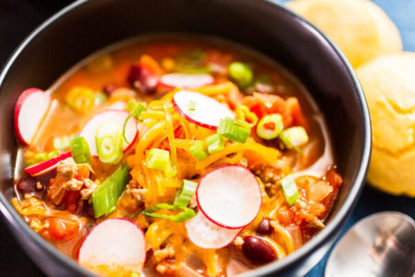 Close up of turkey chili garnished with fresh radishes, green onions and cheddar cheese.