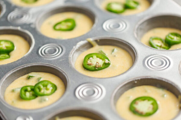Cornbread batter in muffin pans garnished with jalapeno peppers.