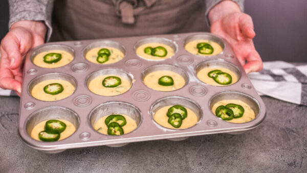 Step by step. Filling metal muffin pan with cornbread batter to bake spicy jalapeno cornbread muffins.