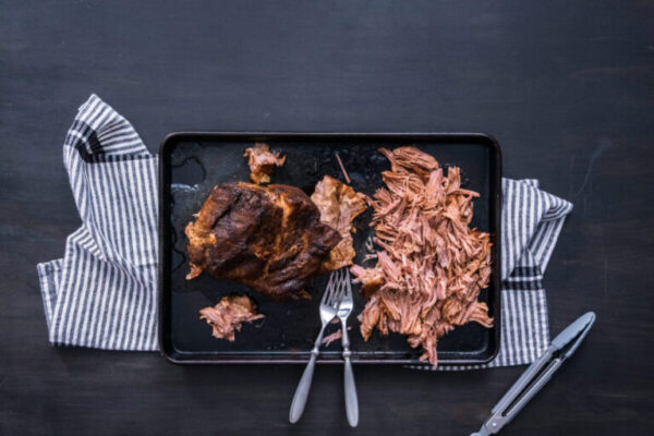 Shredding cooked pork with forks on a baking sheet.