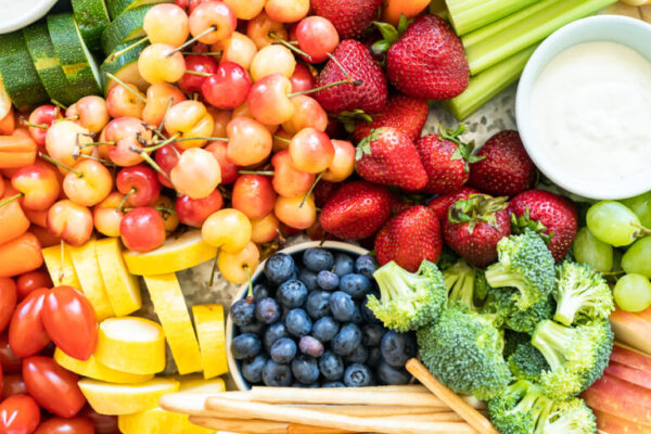 Snack board with fresh fruit, vegetables, crackers, and dips.