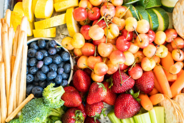 Snack board with fresh fruit, vegetables, crackers, and dips.