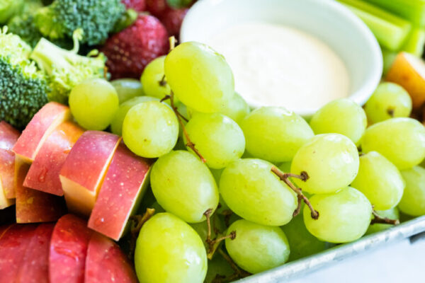 Snack board with fresh fruit, vegetables, crackers, and dips.