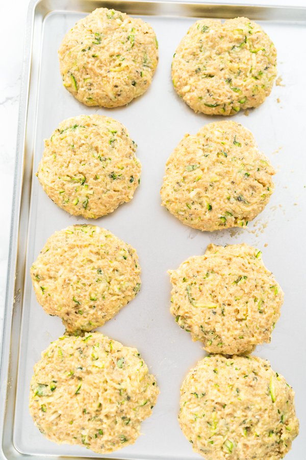 Close-up of raw zucchini cakes showing texture and even spacing on the tray.