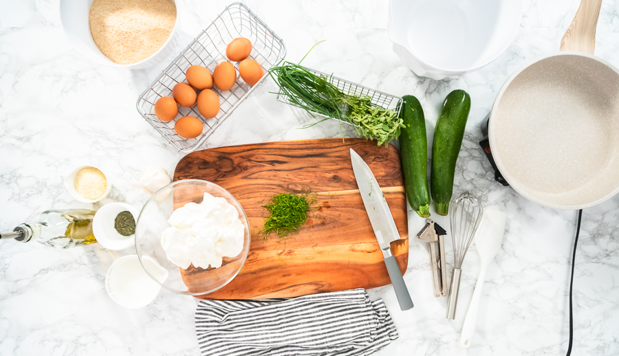 Prepped ingredients on a cutting board including zucchini, garlic, eggs, and cheese.