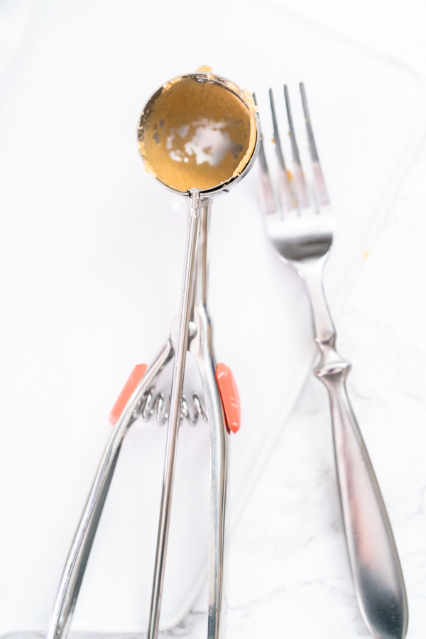 Cookie scoop and fork on a baking sheet for shaping and pressing cookies