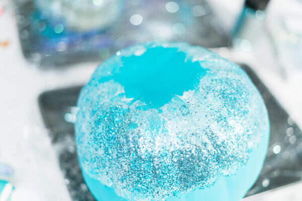 Decorating Halloween craft pumpkin with blue glitter.