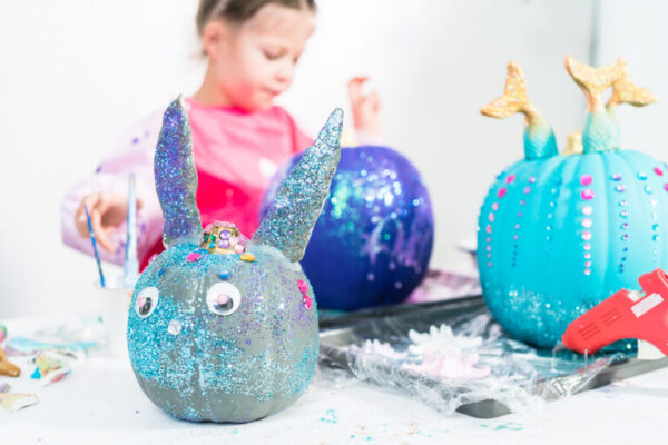 Little girl decorating her Halloween pumpkin with glitter.