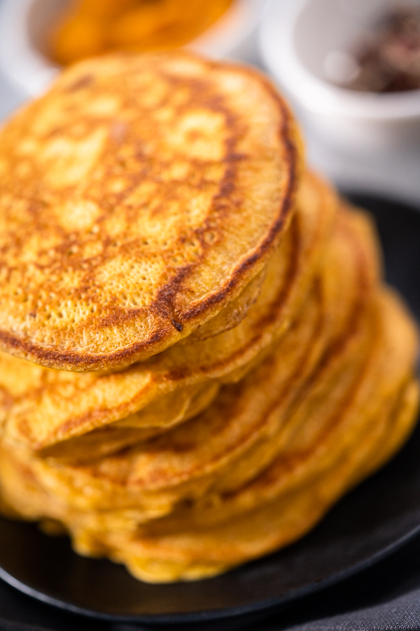 Stack of golden pumpkin pancakes topped with whipped cream and pecans, ideal for brunch.