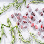 Covering fresh cranberries and rosemary in sugar to decorate chocolate bundt cake with chocolate frosting.