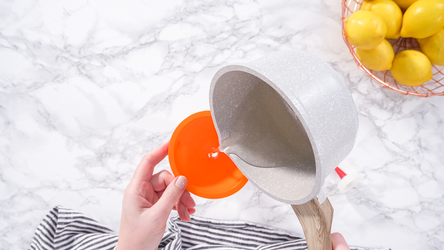 Pouring warm syrup from a saucepan into a funnel over a squeeze bottle.