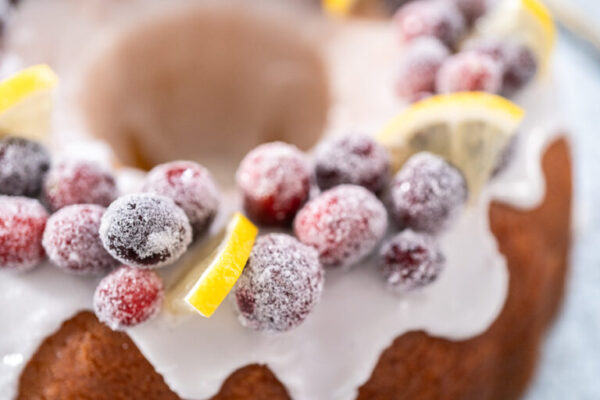 Lemon cranberry bundt cake decorated with sugar cranberries and lemon wedges on a cake stand.