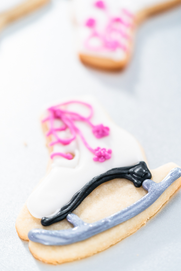 Decorating sugar cookies shaped as figure skates with royal icing.