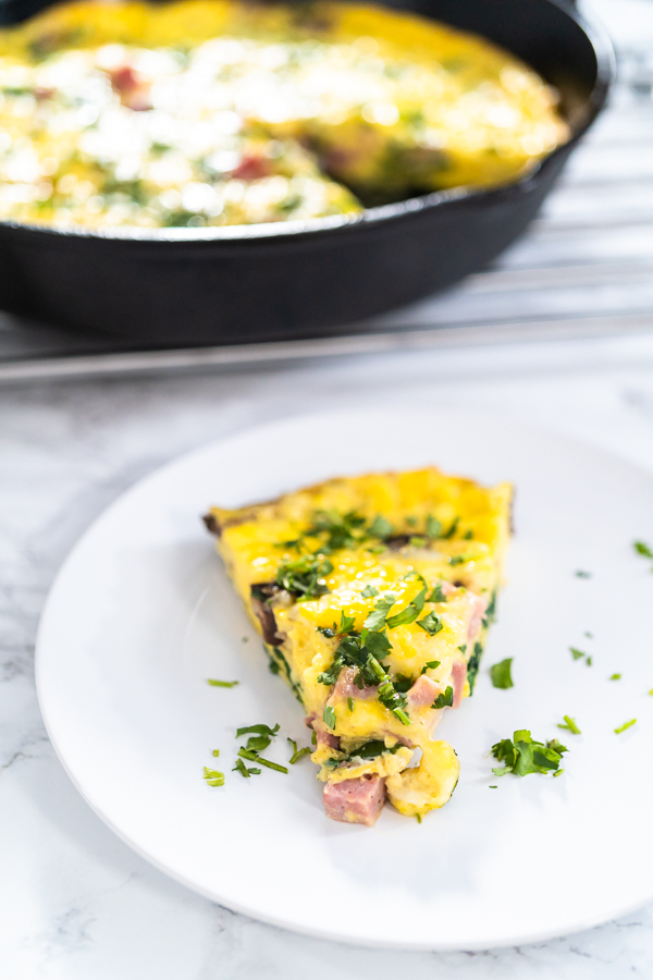 A single wedge of spinach and ham frittata served on a white plate with a sprinkle of herbs.