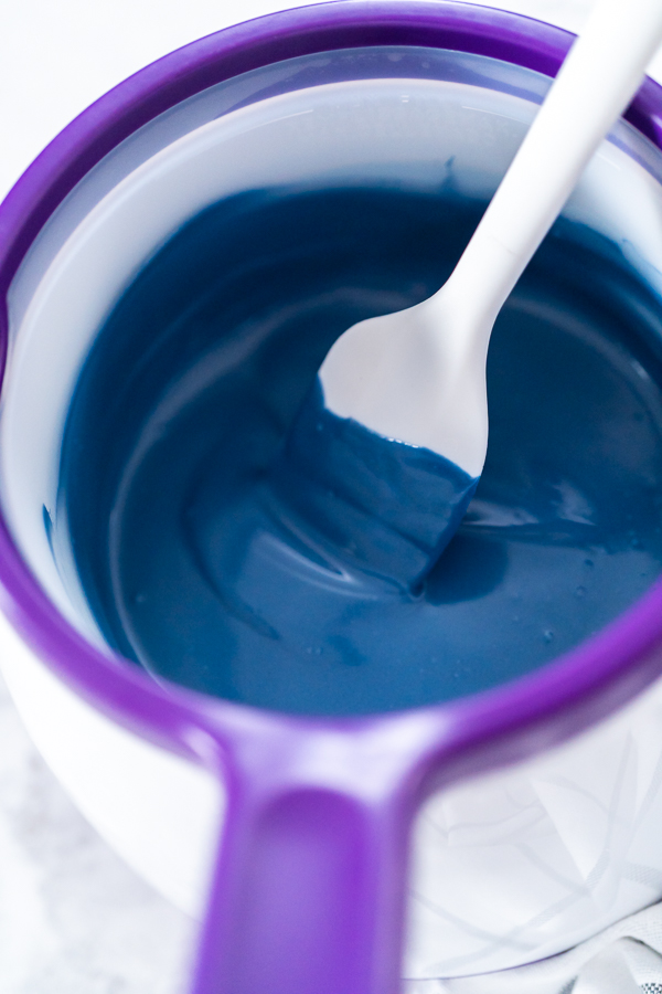 Melted royal blue candy melts in a candy melting pot with a white silicone spatula, ready for dipping pretzel rods.