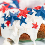 Close-up of a patriotic Bundt cake topped with glossy vanilla glaze and red, white, and blue chocolate stars.