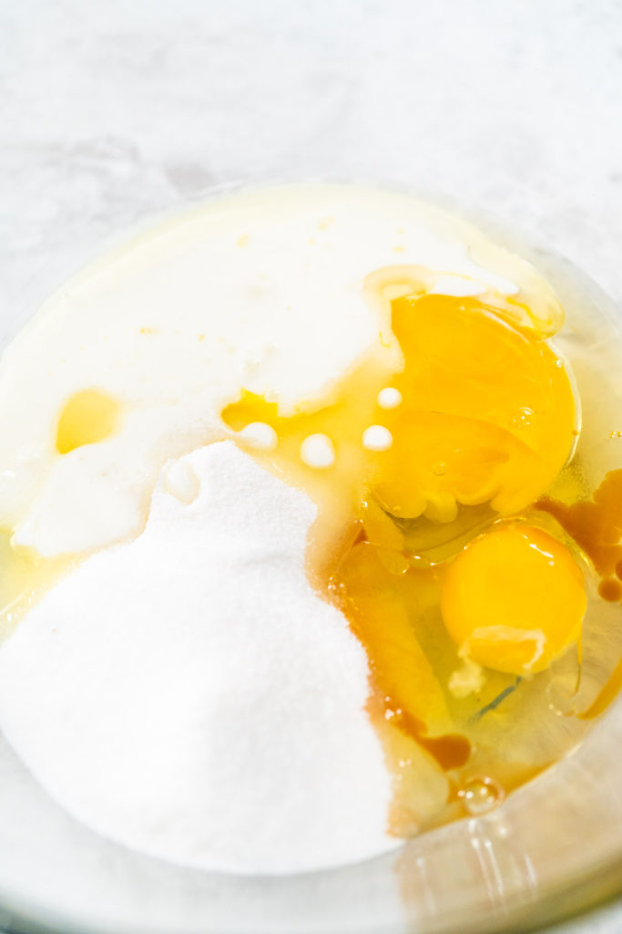 Close-up of eggs, sugar, vanilla extract, oil, and buttermilk in a glass bowl, ready to be mixed for cupcake batter.