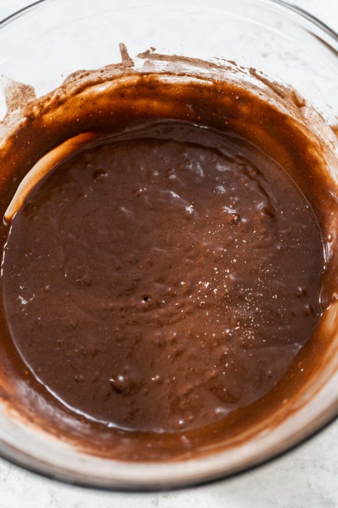 Thick and glossy chocolate cupcake batter swirled in a glass mixing bowl, ready to be scooped into cupcake liners.