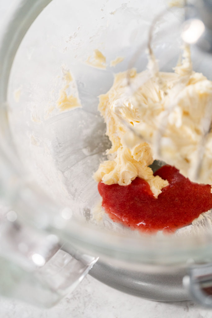 Adding strawberry puree into the bowl with whipped butter and sugar for color and flavor.