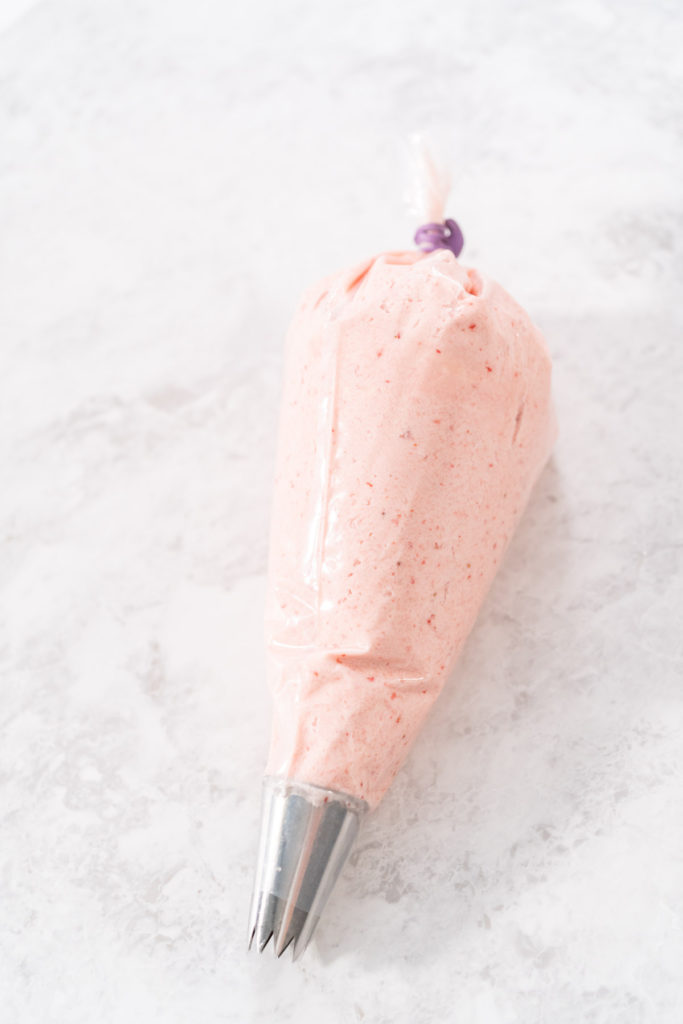 Full piping bag filled with freshly made strawberry buttercream, sealed and ready for decorating.