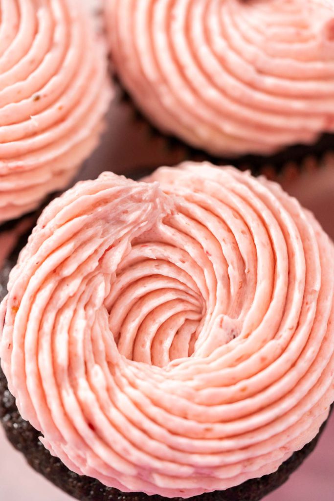Extreme close-up of a chocolate cupcake topped with a perfect swirl of strawberry frosting.