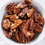 Freshly toasted pecans in a small white bowl.