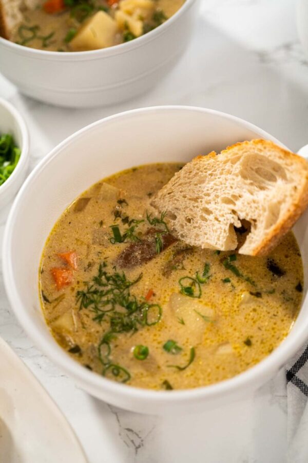 Serving creamy wild mushroom soup made out of dehydrated wild mushrooms in white bowls with sourdough bread.