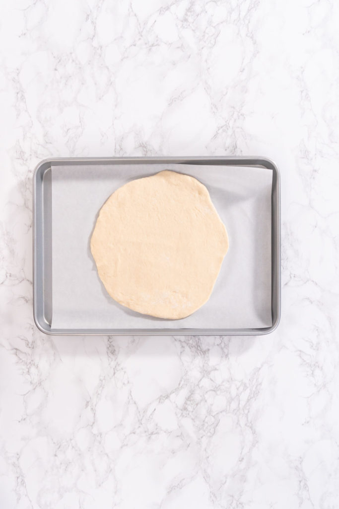 Rolled out round of dough on baking sheet lined with parchment paper, ready for toppings.