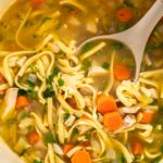 Serving chicken noodle soup with kluski noodles in white ceramic soup bowls.