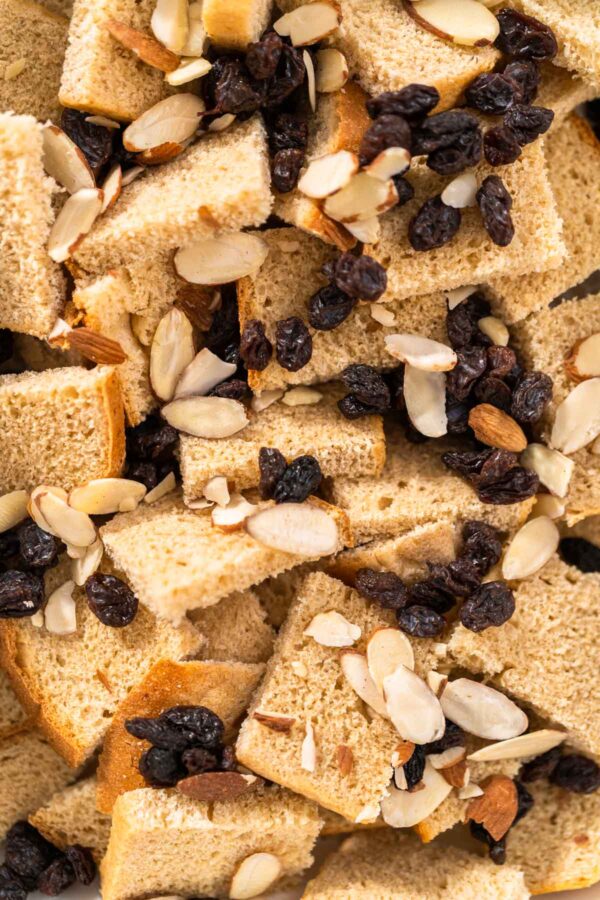 Baking bread pudding with raising and almond slivers in a white casserole dish.