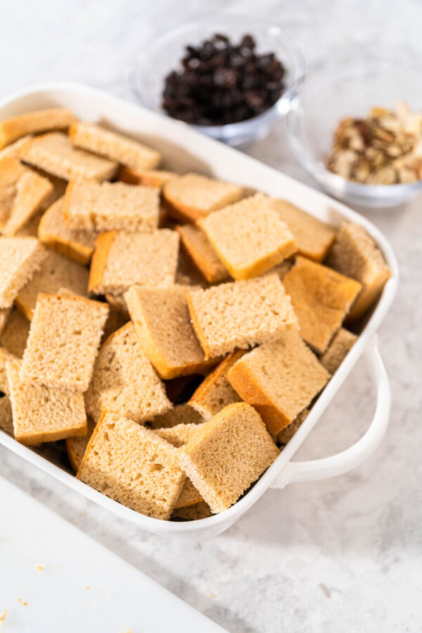 Baking bread pudding with raising and almond slivers in a white casserole dish.