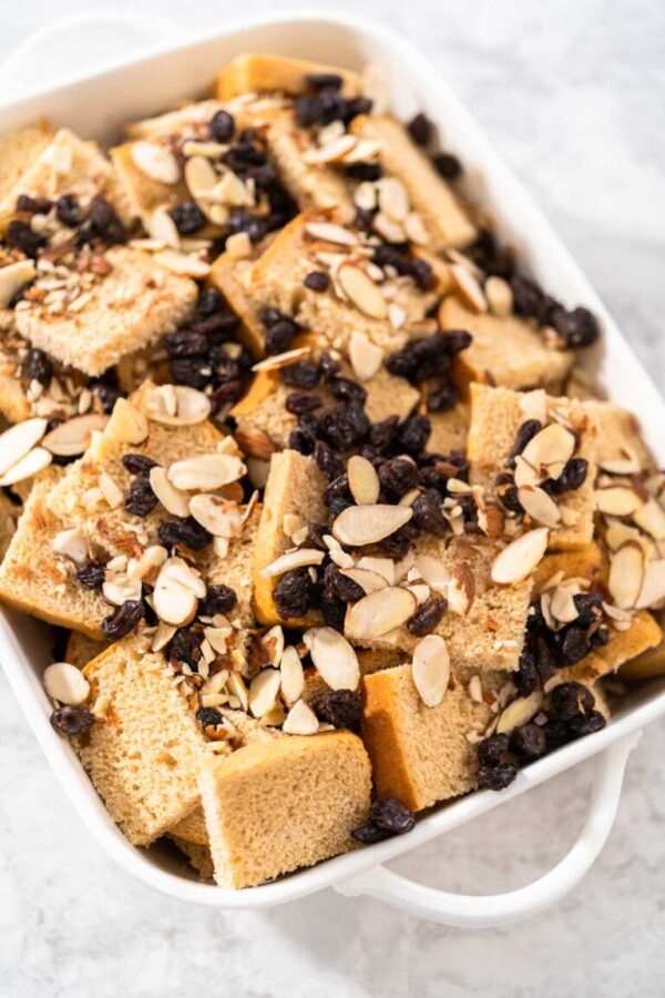 Baking bread pudding with raising and almond slivers in a white casserole dish.