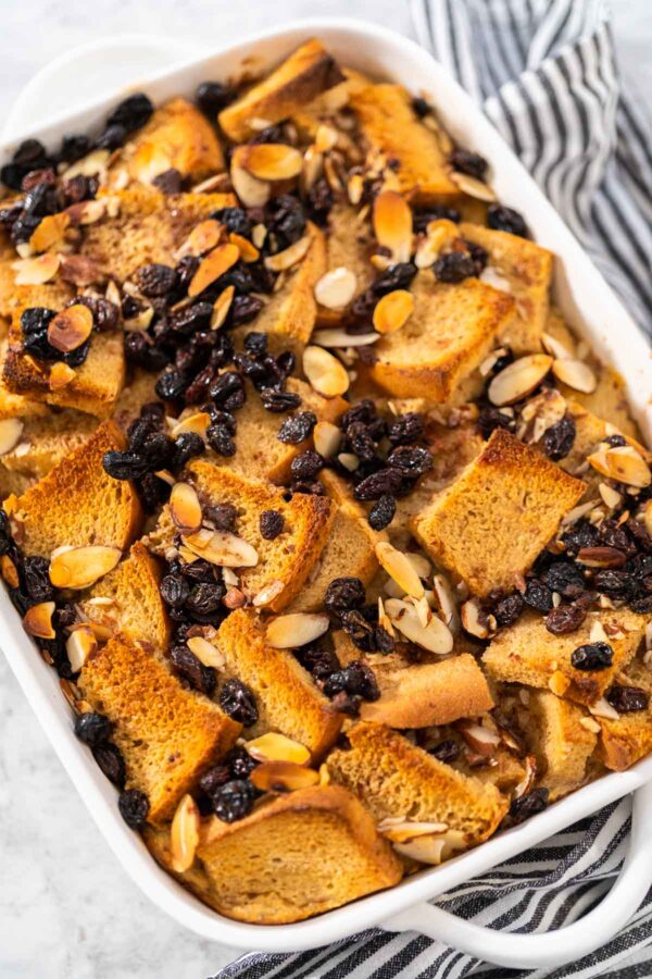 Cooling freshly baked bread pudding with raising and almond slivers in a white casserole dish.