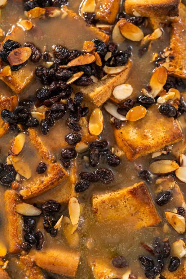 Cooling freshly baked bread pudding with raising and almond slivers in a white casserole dish.