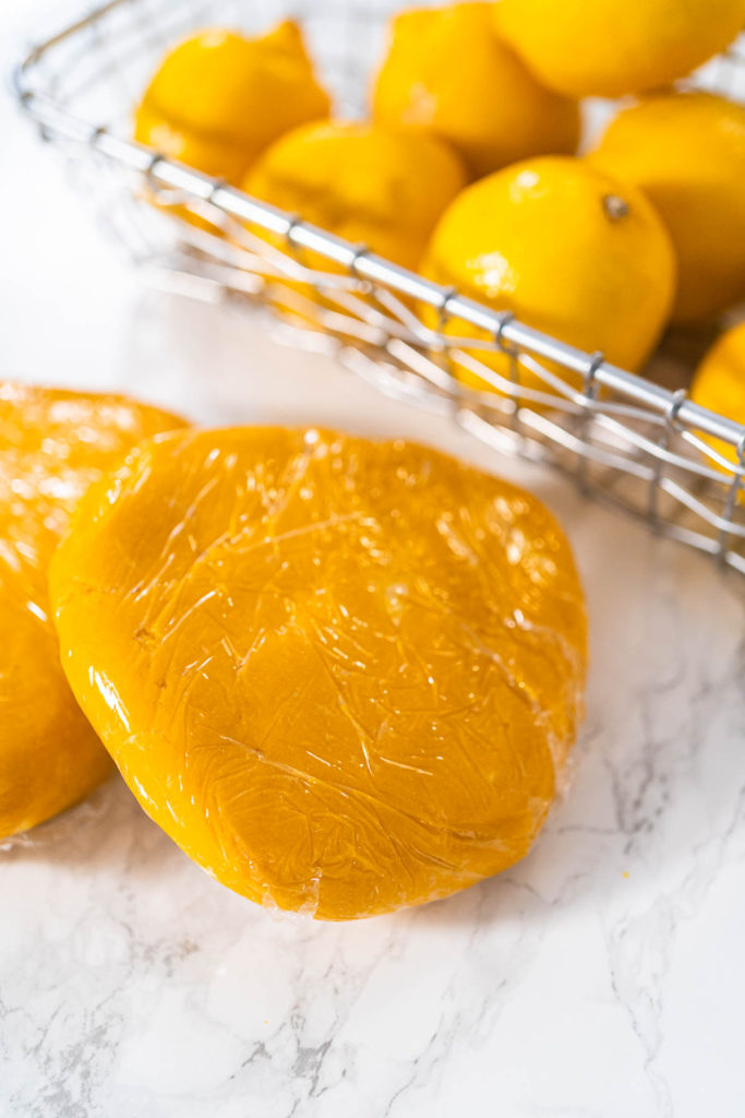 Two disks of yellow cookie dough wrapped in plastic wrap.