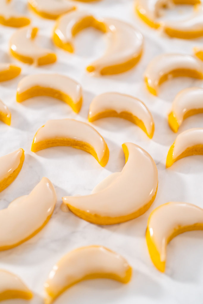 Close-up of glazed lemon cookies drying on parchment.