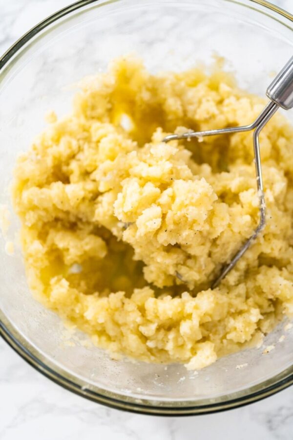 Mashed potatoes. Mashing cooked potatoes in a glass mixing bowl with a potato masher to make mashed potatoes.