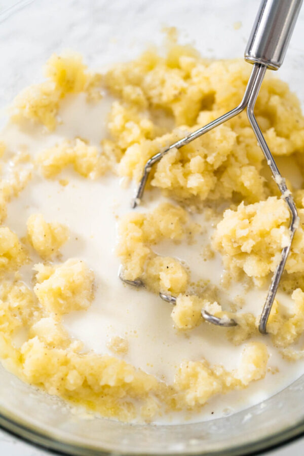Mashed potatoes. Mashing cooked potatoes in a glass mixing bowl with a potato masher to make mashed potatoes.