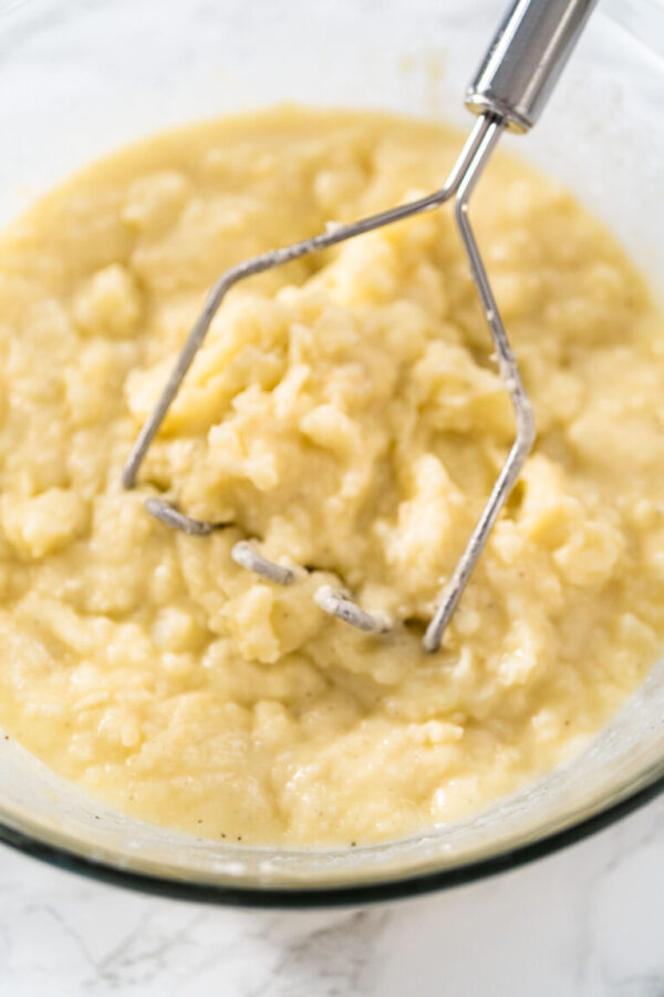 Mashed potatoes. Mashing cooked potatoes in a glass mixing bowl with a potato masher to make mashed potatoes.
