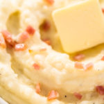 Mashed potatoes. Creamy mashed potatoes garnished with a slice of butter and bacon bits in a bowl.