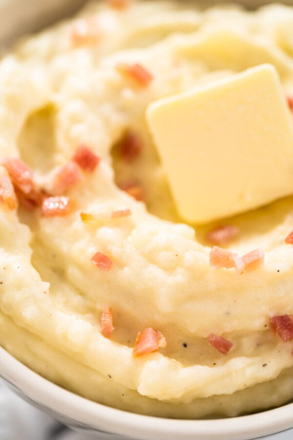 Mashed potatoes. Creamy mashed potatoes garnished with a slice of butter and bacon bits in a bowl.