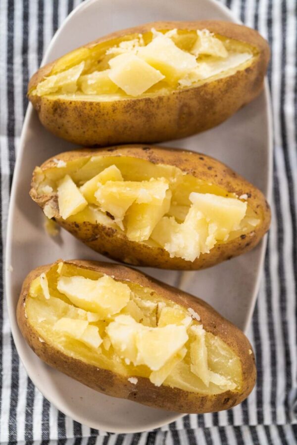 Pressure Cooker Baked Potatoes. Sliced cooked whole potatoes on a white plate to make baked potatoes.