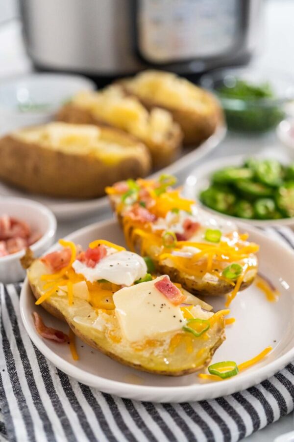 Pressure Cooker Baked Potatoes. Garnished large baked potatoes with butter, sour cream, cheese, and bacon bits on a white plate.
