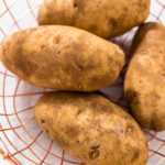 Pressure Cooker Baked Potatoes. Raw potatoes in a wire basket on the kitchen counter.