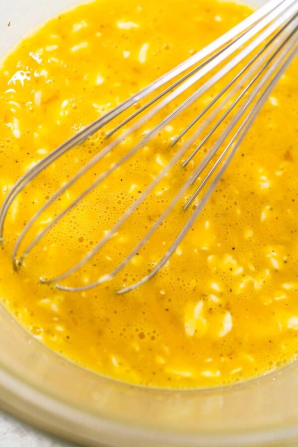 Mixing ingredients with a hand whisk in a glass mixing bowl to make egg bites.