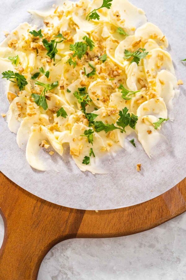 Assembling butter board with vegetables and bread on a round wood cutting board.