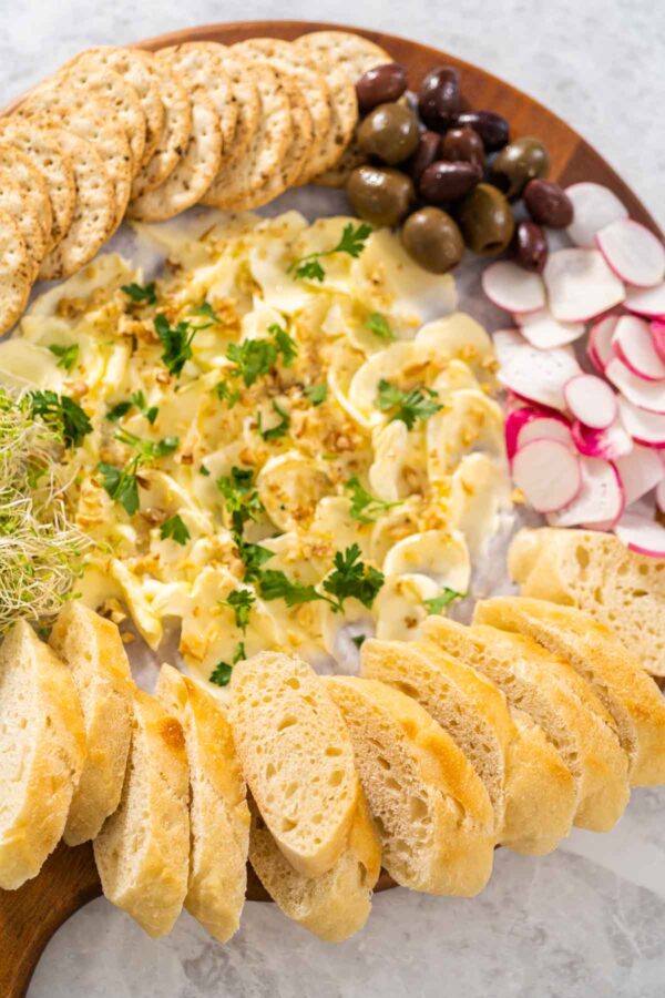 Butter board with vegetables and bread on a round wood cutting board.