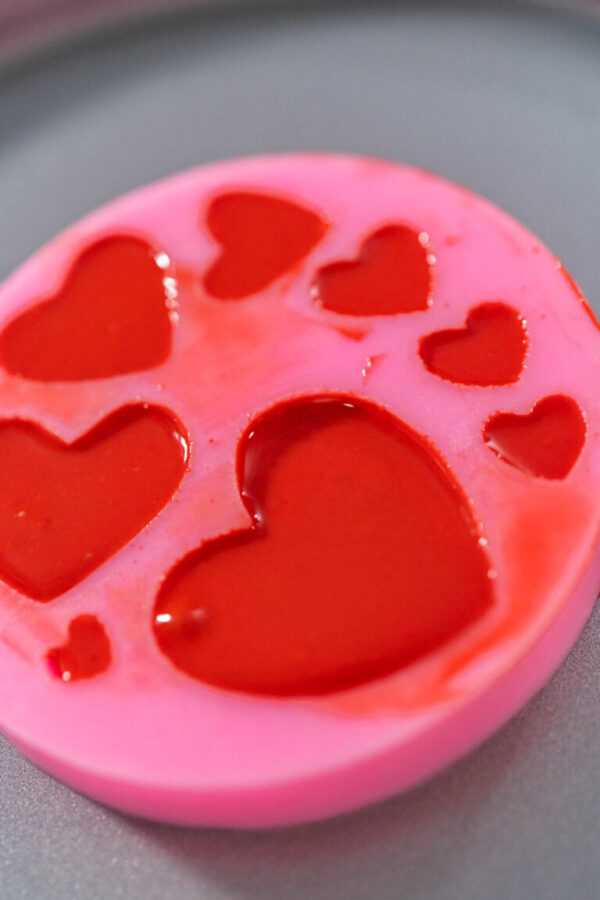 Filling heart silicone chocolate mold with melted chocolate to make chocolate hearts for decorating green fudge.