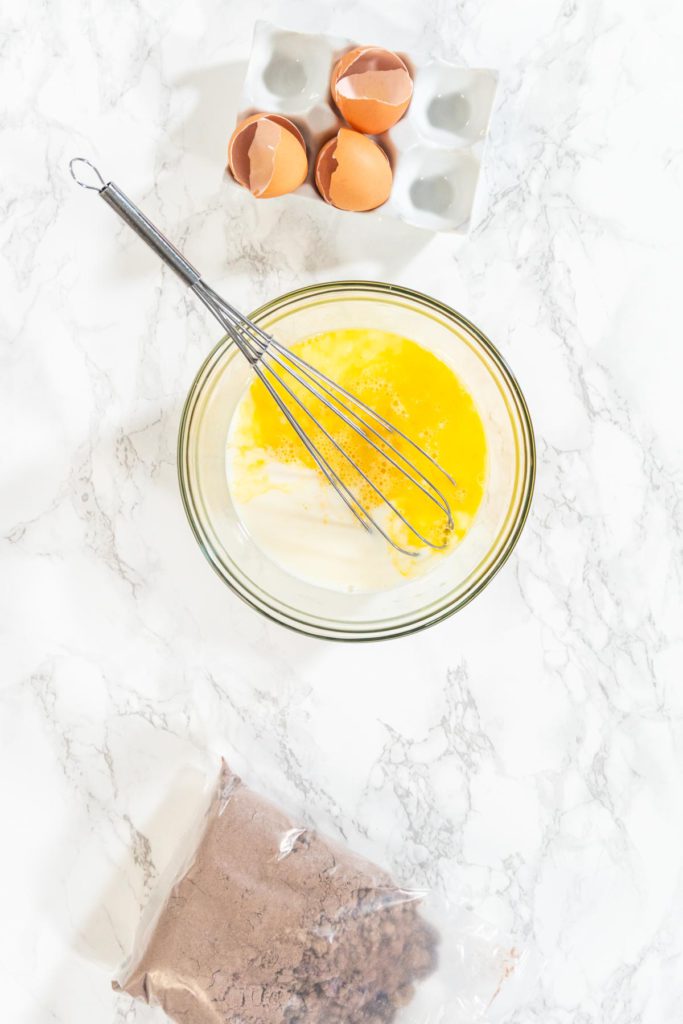 Whisk blending milk and beaten eggs in a clear bowl for cupcake batter.