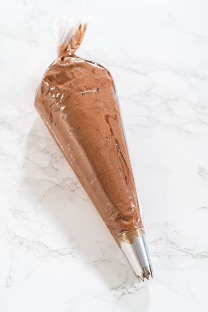 Clear piping bag filled with chocolate frosting, sealed and placed on a clean white surface.